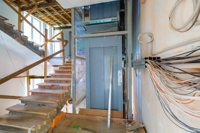 Wall with wires, stairs with temporary wooden railing and elevator in an apartment is during on the construction, remodeling, rebuilding and renovation.